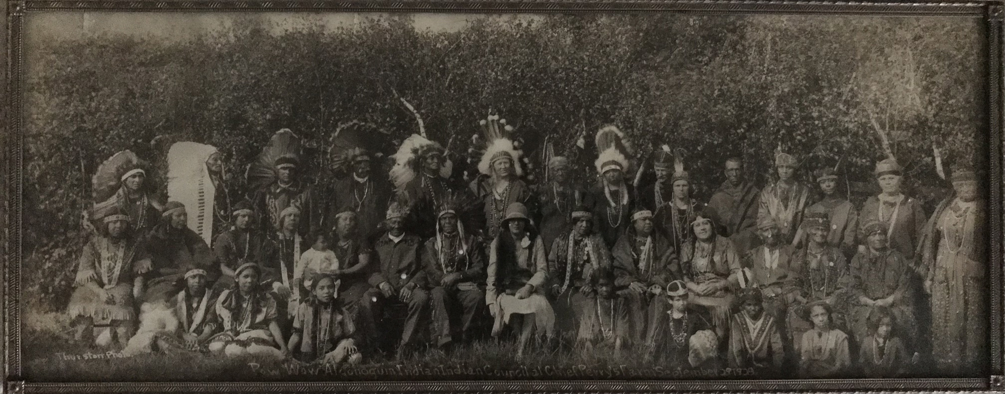 Sepia photograph of a group of people posing for a portrait in a range of North American Indigenous and 1920s-style clothing. Inscription reads, "Pow Wow Algonquin Indian Indian Council at Chief Perrys Farm September 29, 1928."